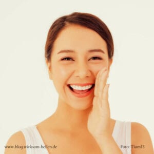 Strahlende junge Frau hält sich die Wange.