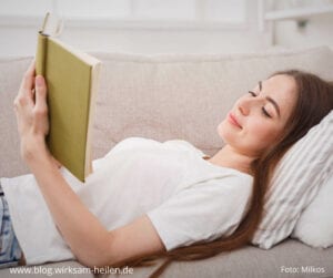 Junge Frau liegt auf dem Sofa und liest ein Buch