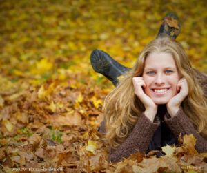 Blonde, junge Frau liegt lachend im Herbstlaub.