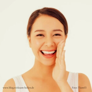 Strahlende junge Frau hält sich die Wange.