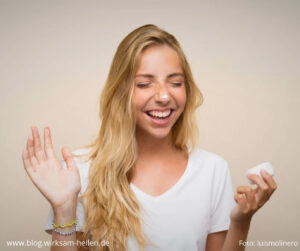 Blonde, junge Frau lacht und hat einen Klecks Gesichts-Creme auf ihrer Nase.